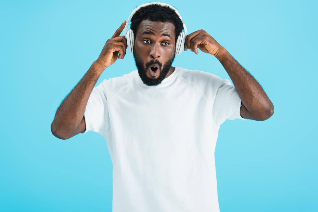 aufgeregter afrikanisch-amerikanischer Mann hört Musik mit Kopfhörern, isoliert auf blauem Grund - Foto, Bild