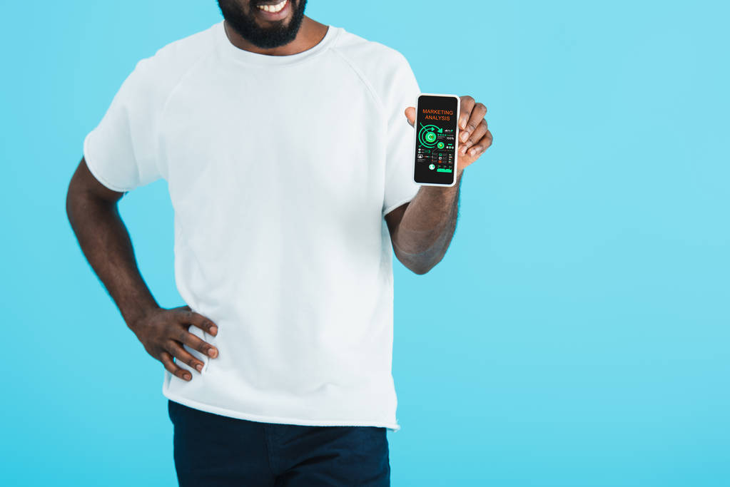 обрізаний вид на афроамериканця, що показує смартфон із додатком маркетингового аналізу, ізольований на синьому
 - Фото, зображення