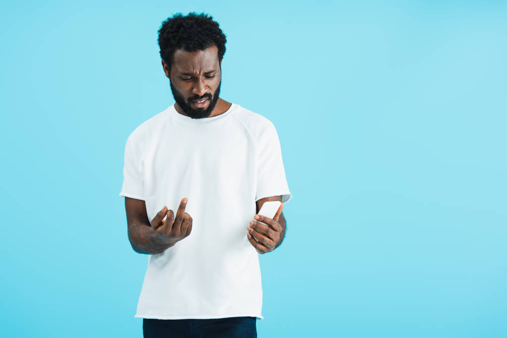 сердитый африканский американец, показывающий средний палец смартфону, изолированный на голубом
 - Фото, изображение