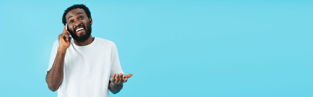 χαμογελαστός Αφρικανός Αμερικανός άνθρωπος με την χειρονομία των ώμων μιλάει στο smartphone, απομονωμένη στο μπλε - Φωτογραφία, εικόνα