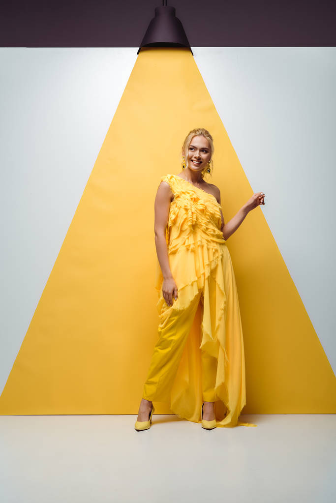 Gelukkig blond meisje glimlachend terwijl poseren en gebaren op wit en geel  - Foto, afbeelding