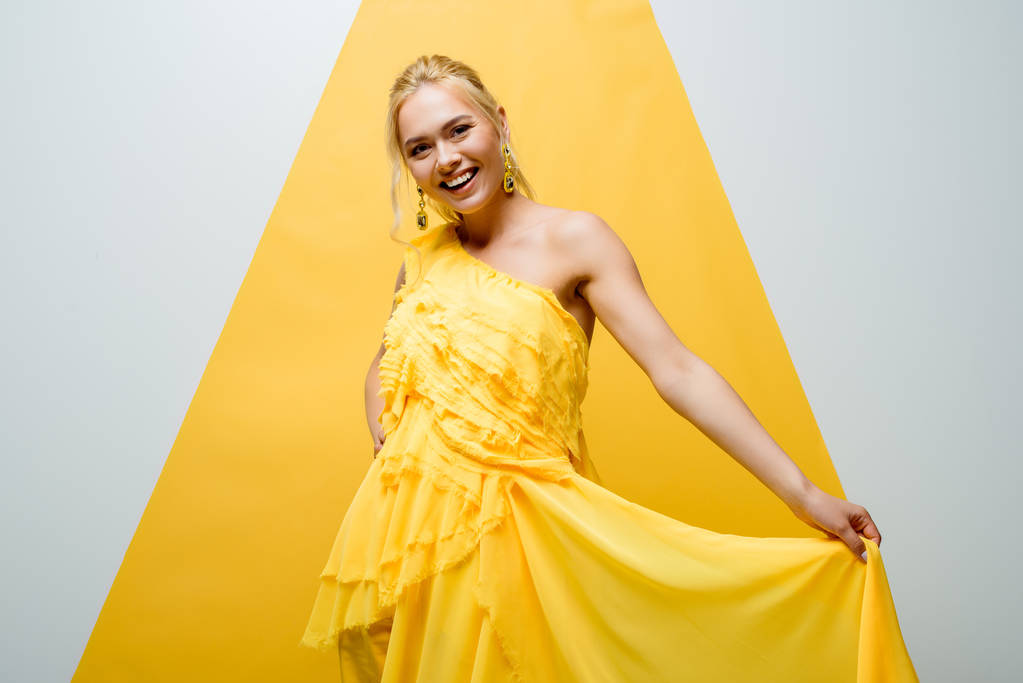 heureuse fille blonde souriant tout en posant et en regardant la caméra sur blanc et jaune
  - Photo, image