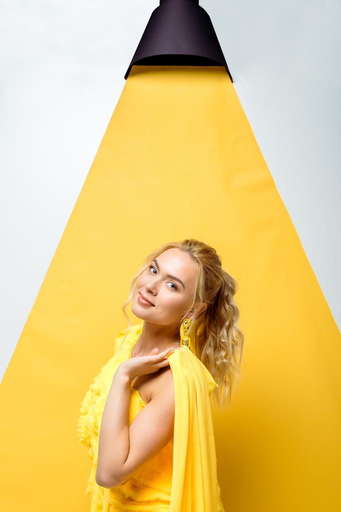 ελκυστική νεαρή γυναίκα κοιτάζοντας την κάμερα και ποζάρει σε λευκό και κίτρινο  - Φωτογραφία, εικόνα