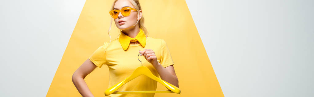 tiro panorâmico de mulher atraente em óculos de sol segurando cabide em branco e amarelo
  - Foto, Imagem