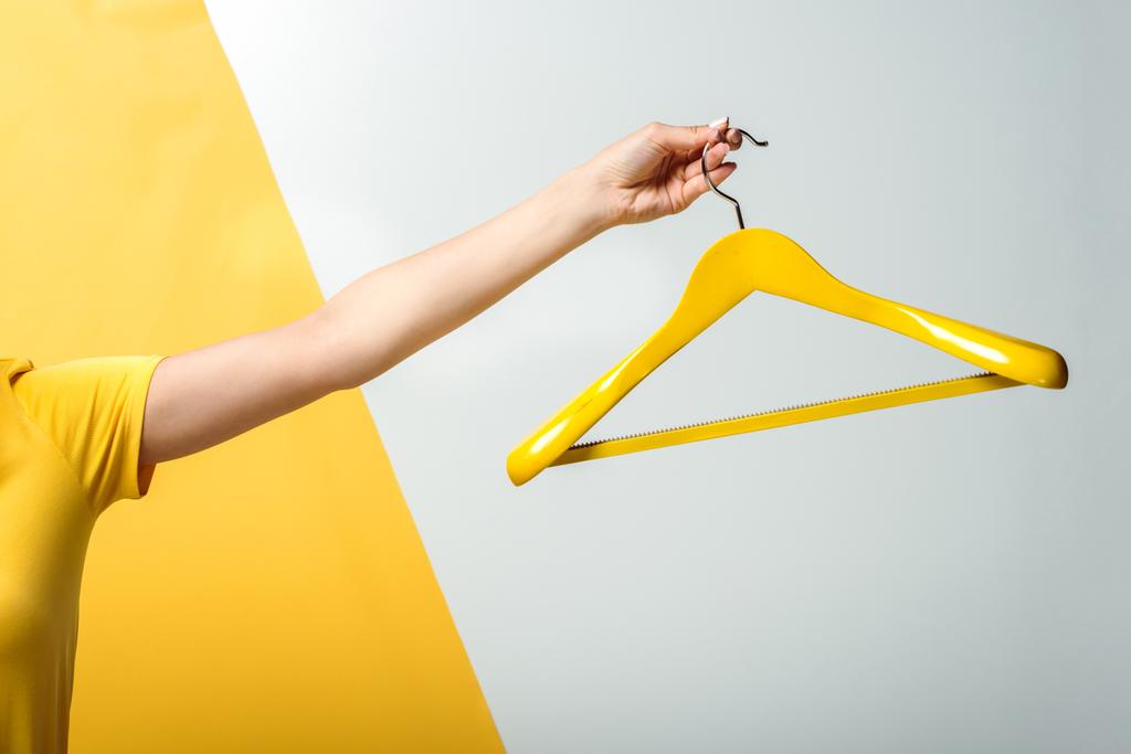 cropped view of woman holding wooden hanger on white and yellow  - Photo, Image