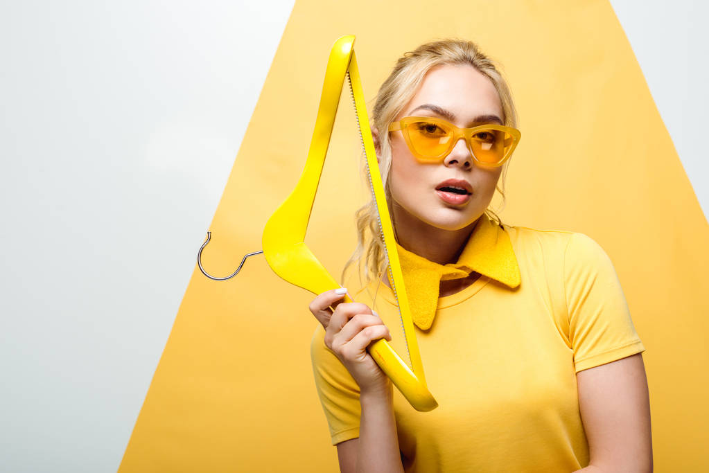 attraente donna bionda in occhiali da sole che tiene appendino in legno su bianco e giallo
  - Foto, immagini