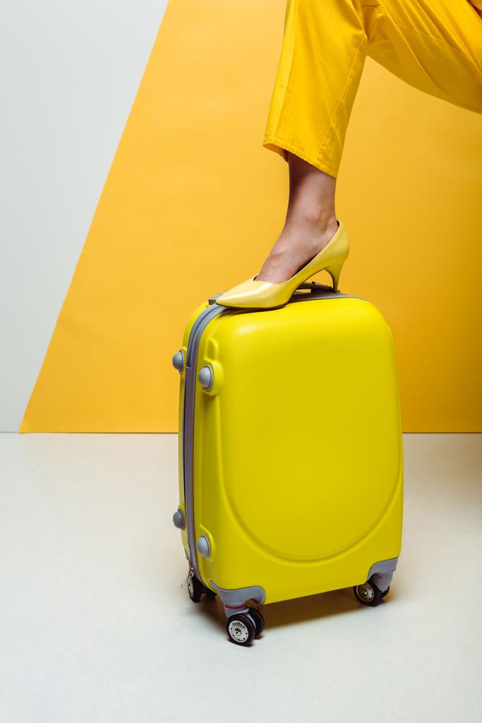 περικομμένη όψη της κομψούς γυναίκας στέκεται στη βαλίτσα σε λευκό και κίτρινο  - Φωτογραφία, εικόνα