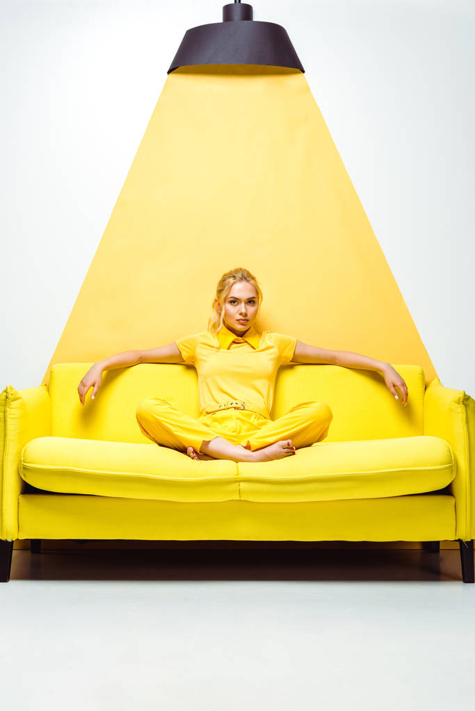  ξανθιά κορίτσι κάθεται στον καναπέ με ξυπόλητη σε λευκό και κίτρινο  - Φωτογραφία, εικόνα