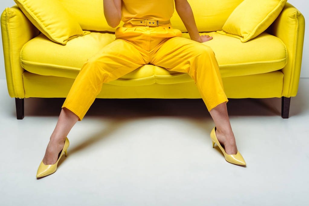 обрезанный вид на стильную молодую женщину на каблуках, сидящую на диване с подушками на белом
  - Фото, изображение