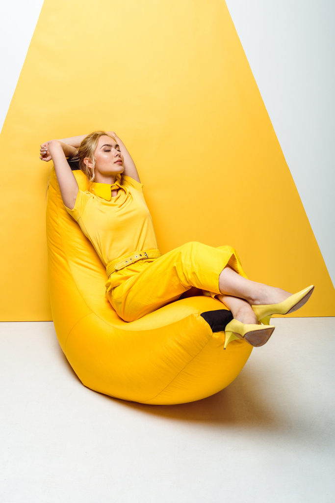 atractiva chica rubia con los ojos cerrados sentado en la silla bolsa de frijol en blanco y amarillo
  - Foto, imagen