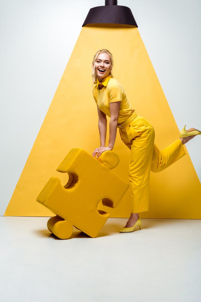 fröhliche blonde Frau hält großes weiches Puzzleteil auf weiß und gelb  - Foto, Bild