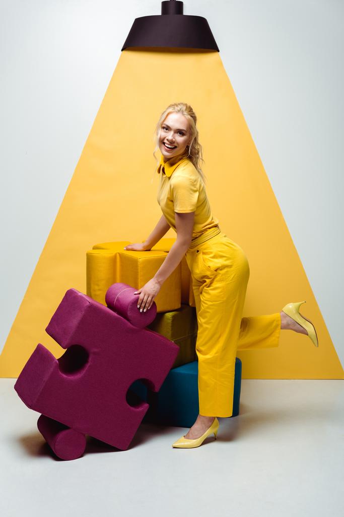 Szczęśliwa kobieta pozowanie w pobliżu kolorowych miękkich puzzli na białym i żółtym  - Zdjęcie, obraz