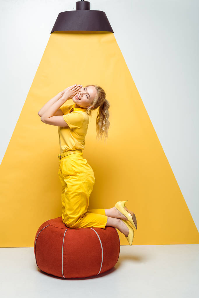 menina loira alegre sorrindo perto de fezes acolchoadas vermelhas em branco e amarelo
  - Foto, Imagem