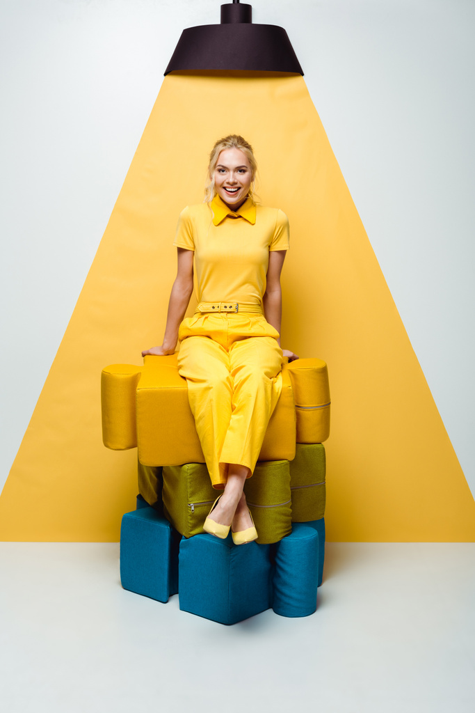 白と黄色の大きな柔らかいパズルのピースに座って幸せなブロンドの女性  - 写真・画像