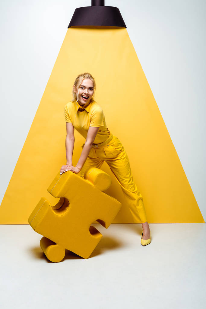 gelukkige blonde vrouw houdt grote zachte puzzel stuk op wit en geel  - Foto, afbeelding
