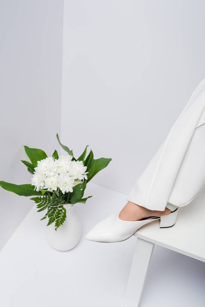 vista cortada da mulher perto do vaso com flores no branco
  - Foto, Imagem