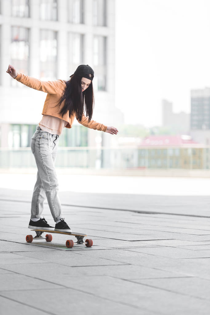 beautiful young woman with outstretched hands riding on skateboard in city - Photo, Image