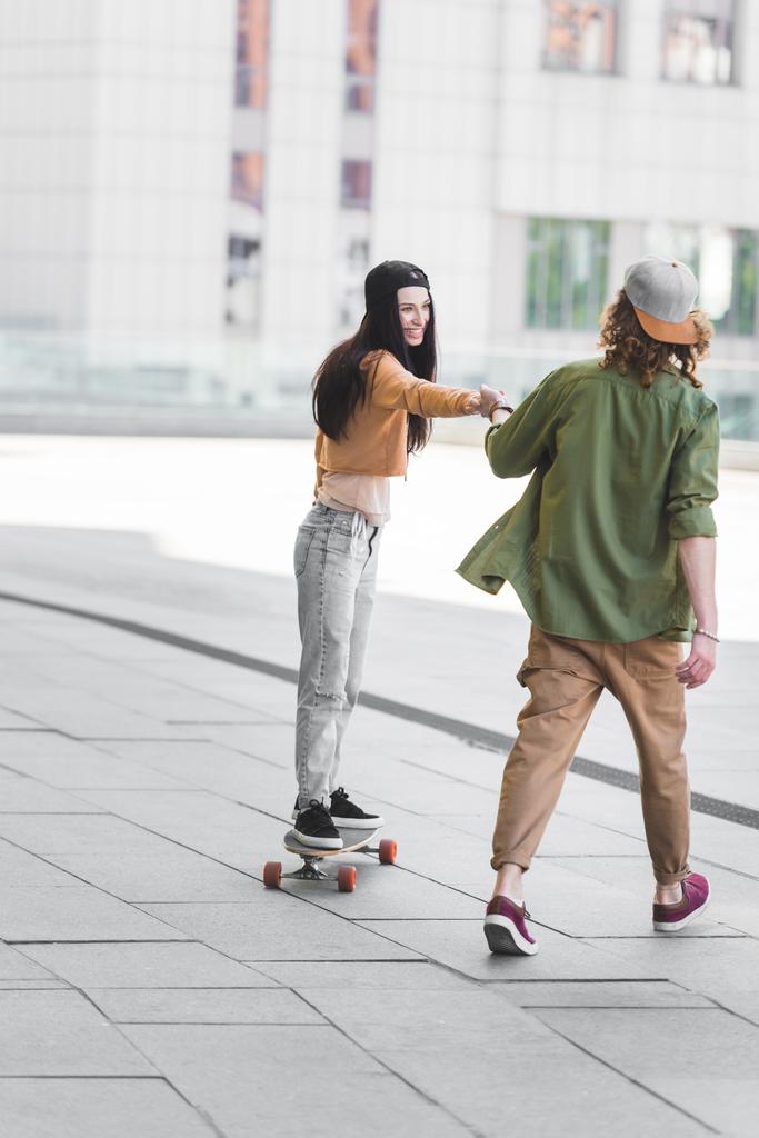 beautiful woman holding hands with man, riding on skateboard in city - Photo, Image