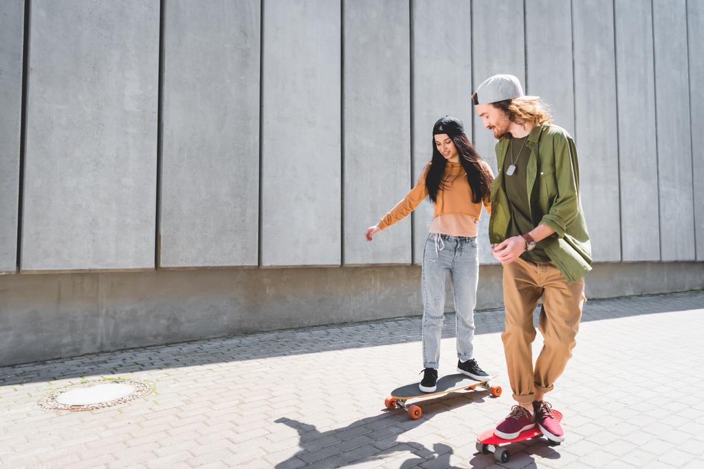 glücklicher Mann hält Händchen mit schöner Frau, fährt auf Skateboard in der Nähe von Betonmauer - Foto, Bild