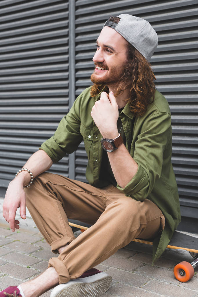 hombre alegre sentado en el monopatín en la calle, mirando hacia otro lado
 - Foto, Imagen
