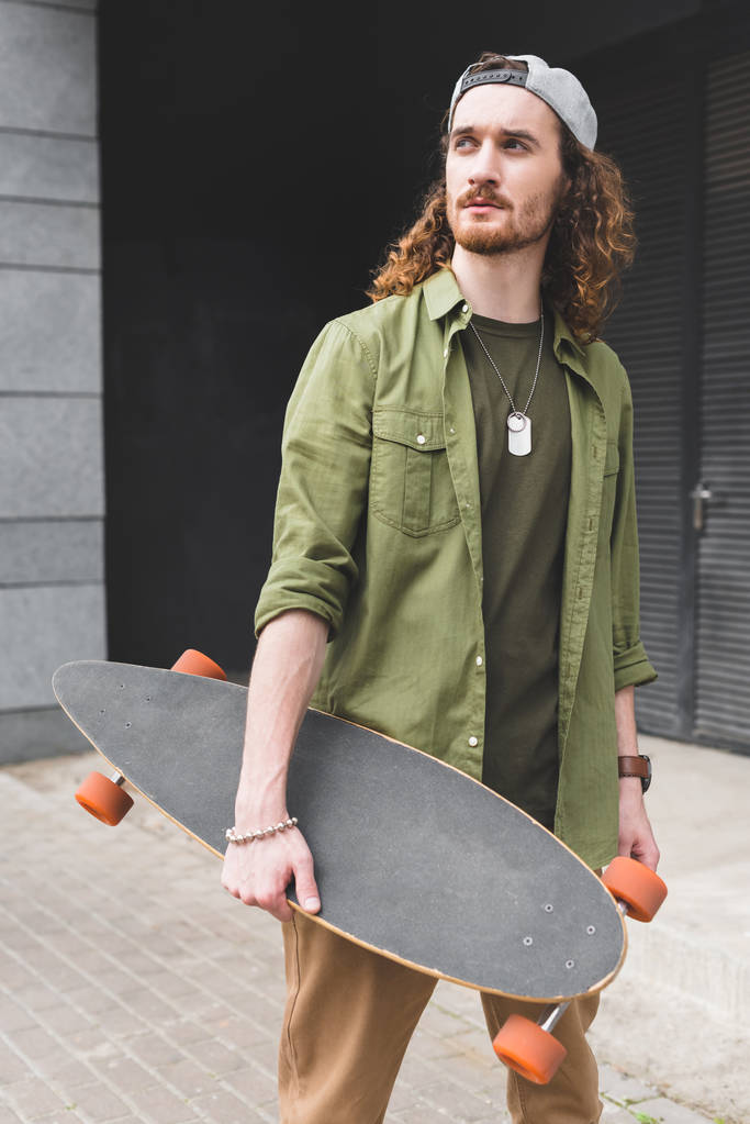calm man holding skateboard in hand, looking away - Photo, Image