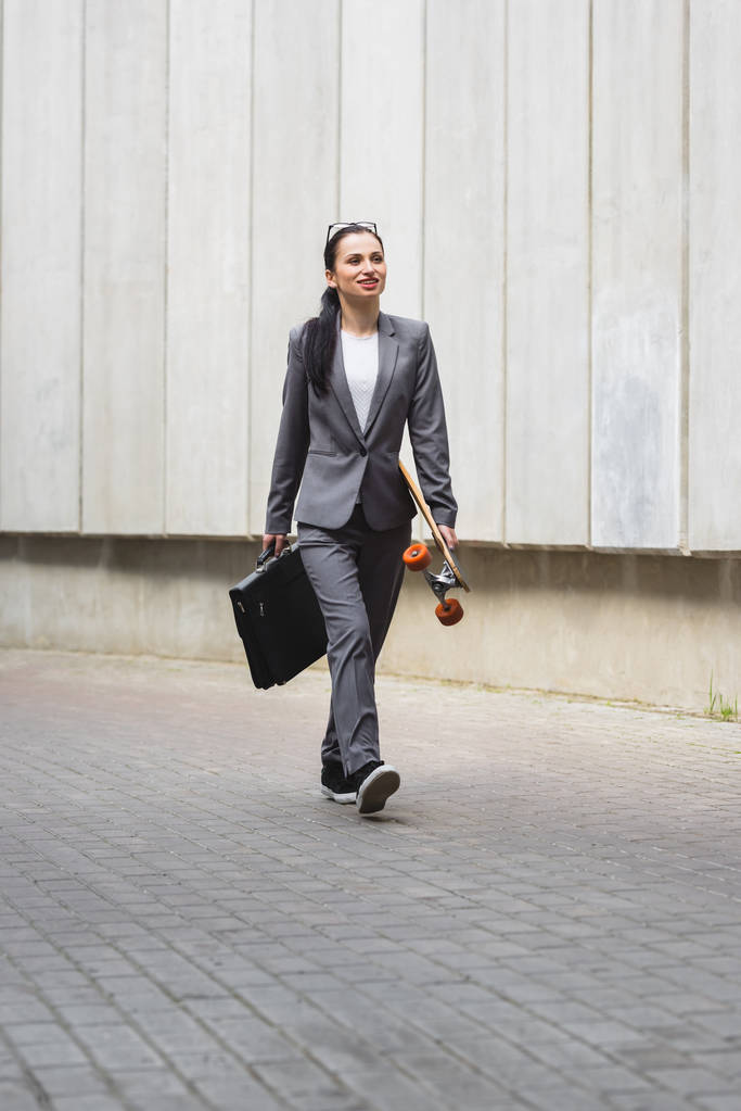 femme d'affaires heureuse en tenue formelle marchant sur la rue avec planche à roulettes à la main
 - Photo, image