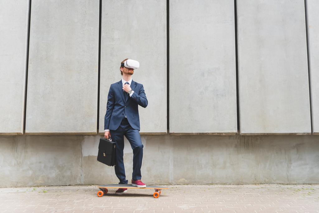 zakenman in formele slijtage en VR-headset staande in de buurt van Longboard op betonnen muur achtergrond - Foto, afbeelding