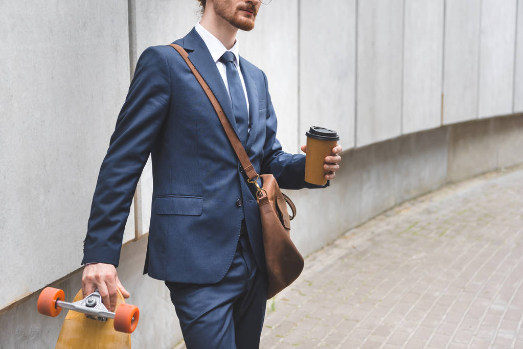 обрізаний вид бізнесмена в офіційному одязі, що тримає скейтборд і паперову чашку в руці
 - Фото, зображення