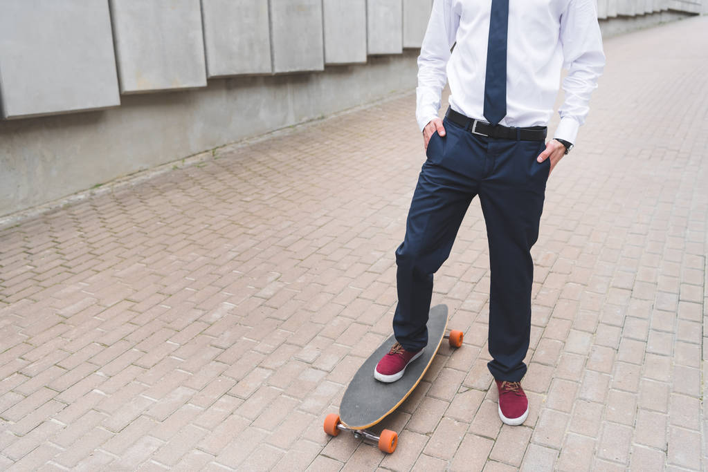 スケートボードに立つフォーマルな服装でビジネスマンのトリミングされたビュー - 写真・画像