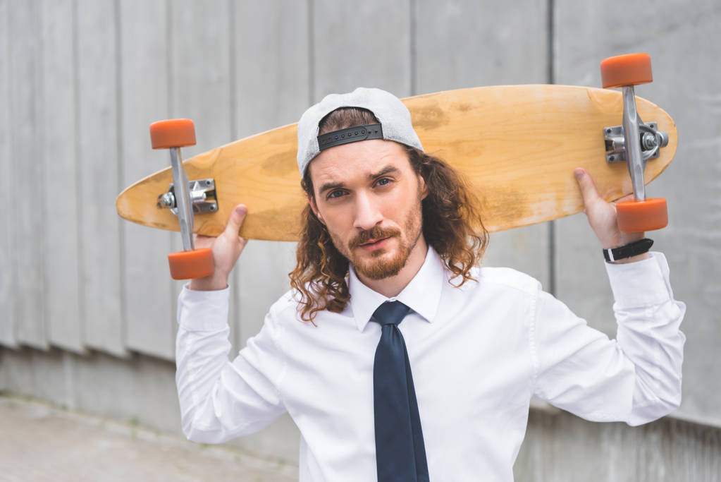 портрет спокойного бизнесмена, стоящего со скейтбордом в руках и смотрящего в камеру
 - Фото, изображение