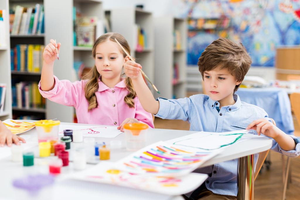 schattige kinderen houden penselen kleurrijke gouache potten en papieren  - Foto, afbeelding