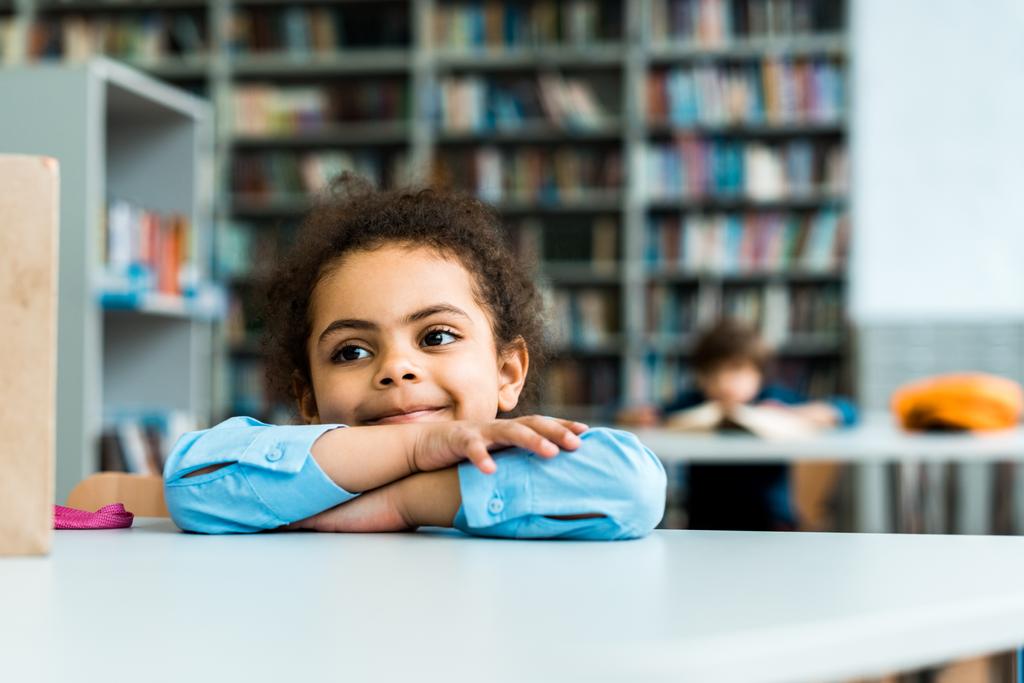 happy african american kid sitting and smiling in library  - Photo, Image
