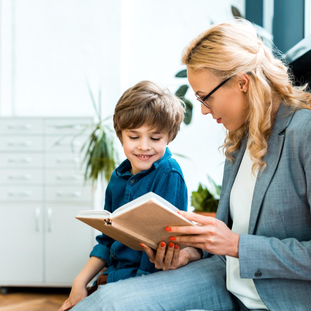 приваблива жінка в окулярах сидить і читає книгу з щасливою дитиною
  - Фото, зображення