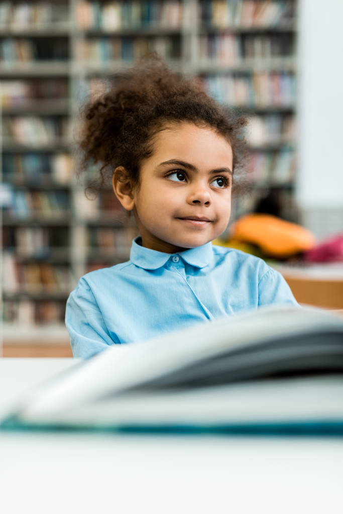 вибірковий фокус щасливої афроамериканської дитини, яка посміхається біля книги на столі
  - Фото, зображення