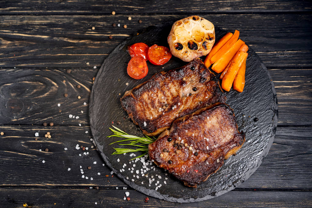 juicy piece of fried meat lies on a stone plate against a black wooden table - Photo, Image