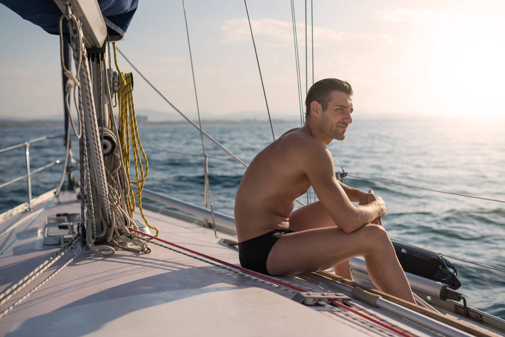 Porträt eines jungen Mannes entspannt auf einem Segelboot bei Sonnenuntergang. - Foto, Bild
