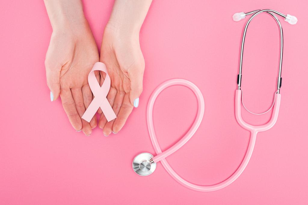 cropped view of woman holding pink breast cancer sign in hands near stethoscope on pink background - Photo, Image