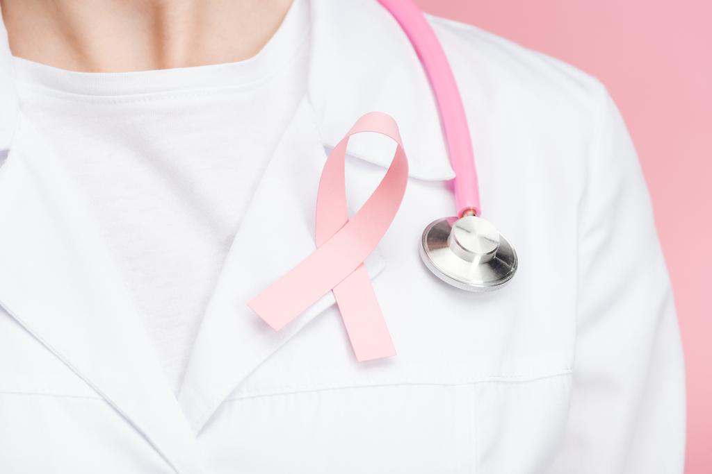 ピンクの乳癌の徴候と聴診器がピンクで隔離された白いコートの医師のクローズアップビュー - 写真・画像