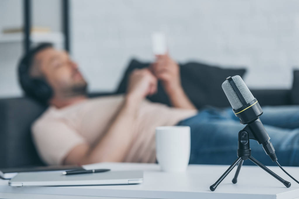вибірковий фокус людини мікрофон на столі біля людини, що лежить на дивані і використовує смартфон
 - Фото, зображення