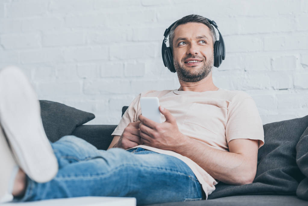 selective focus of cheerful man in headphones looking away while holding smartphone - Photo, Image
