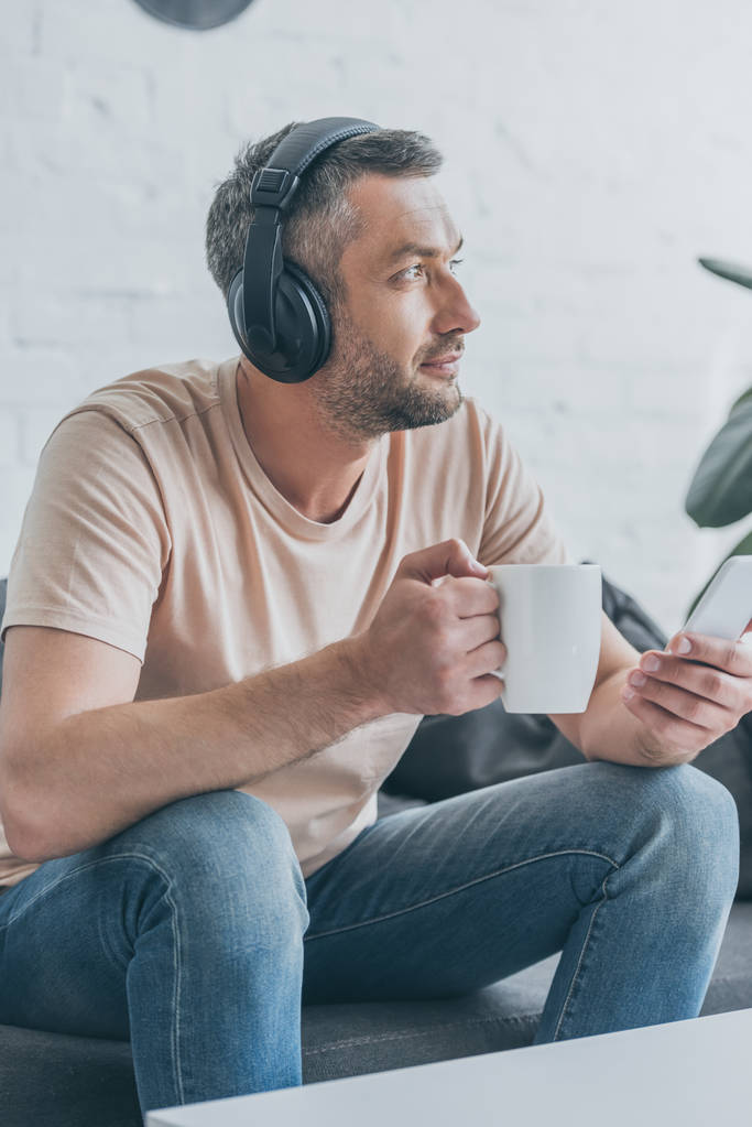 pensive man in headphones holding smartphone and looking away - Photo, Image