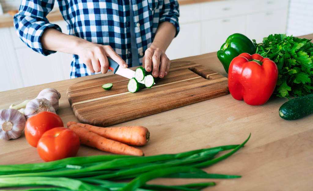 Kadın elleri mutfakta sebze kesiyor. Sağlıklı yemek pişiren kadın. Kesme tahtasında taze sebzeler var. Yemek pişirme konsepti. Diyet. Sağlıklı ve vegan yaşam tarzı. Evde yemek pişirmek. Yemek hazırlayın - Fotoğraf, Görsel