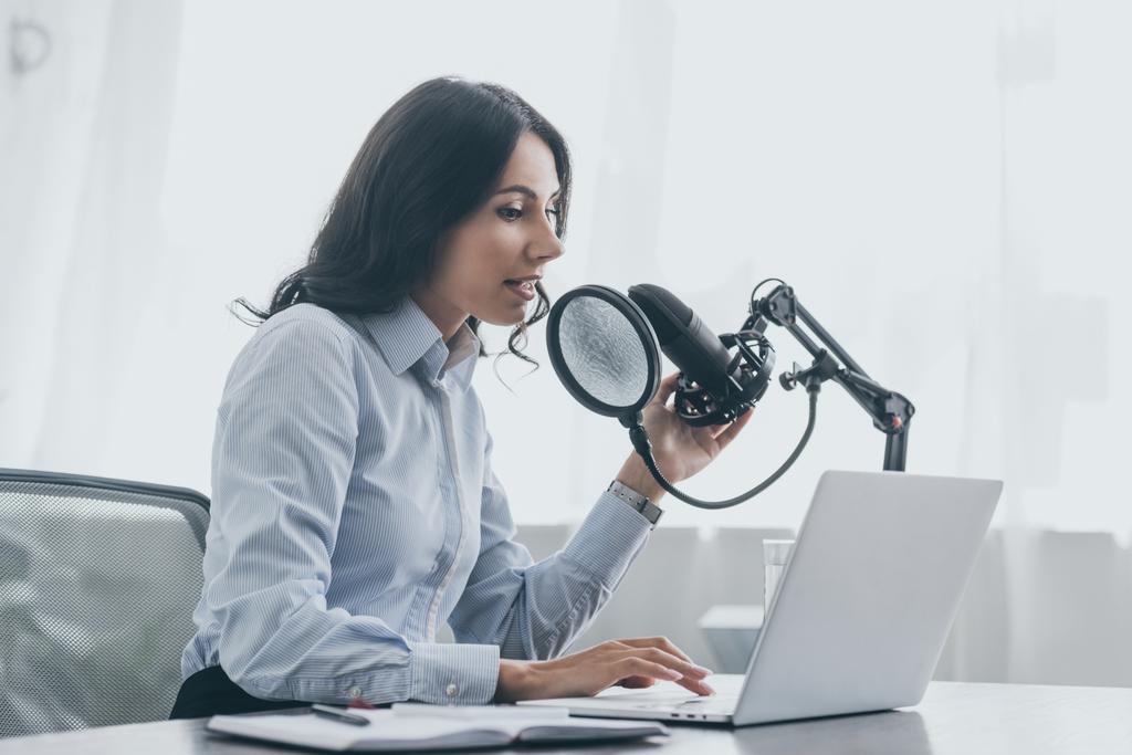 симпатичная радиоведущая с ноутбука во время разговора в микрофон на рабочем месте в радиовещательной студии
 - Фото, изображение