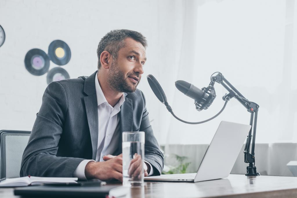 anfitrião de rádio sorrindo falando em microfone enquanto sentado perto de laptop no estúdio de radiodifusão
 - Foto, Imagem