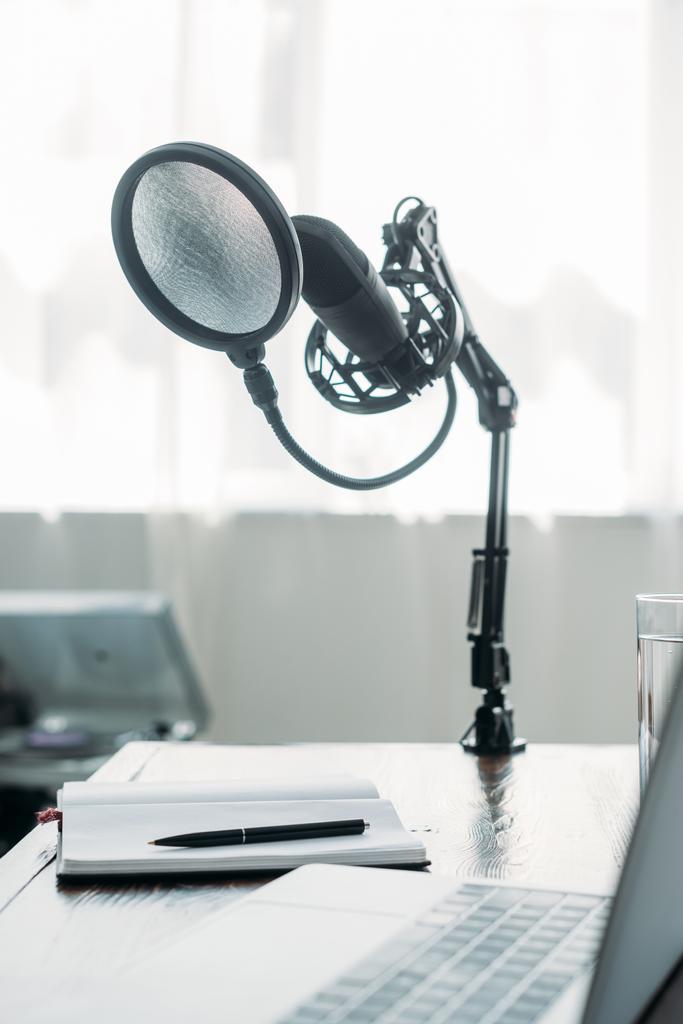 selective focus of microphone fixed on table near laptop in broadcasting studio - Photo, Image