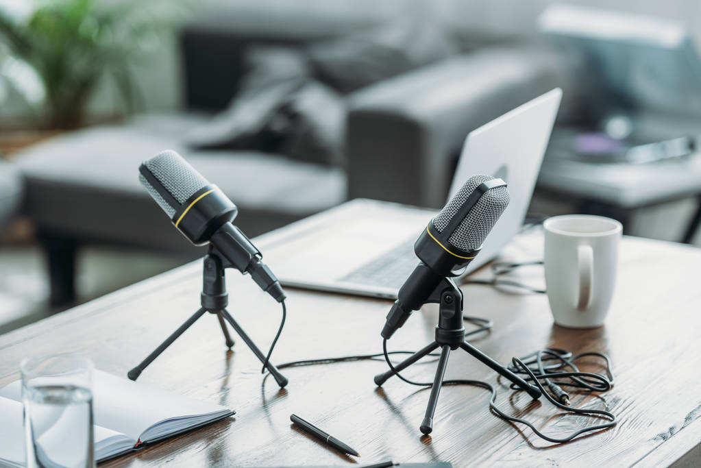 zwei Mikrofone, Laptop, Notizbuch und Kaffeetasse auf Holztisch im Radiostudio - Foto, Bild