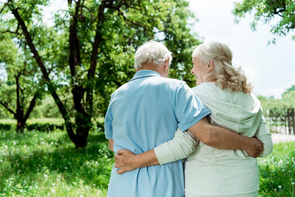 atrás ver jubilado hombre abrazando senior feliz esposa en verde parque
  - Foto, imagen