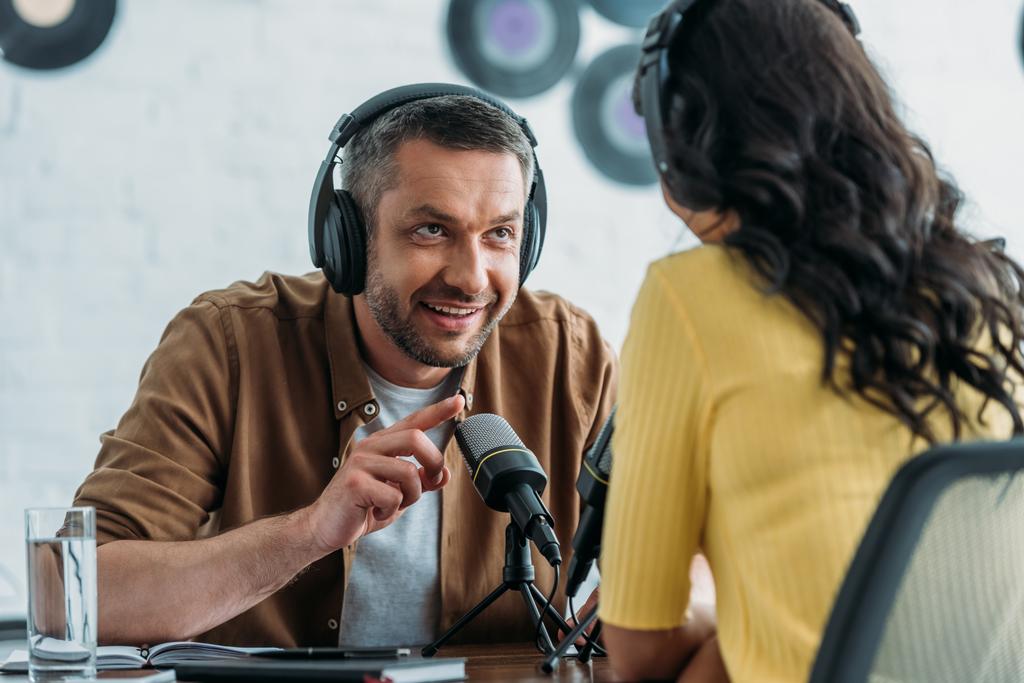 улыбающийся радиоведущий жестикулирует во время разговора с коллегой в студии вещания
 - Фото, изображение