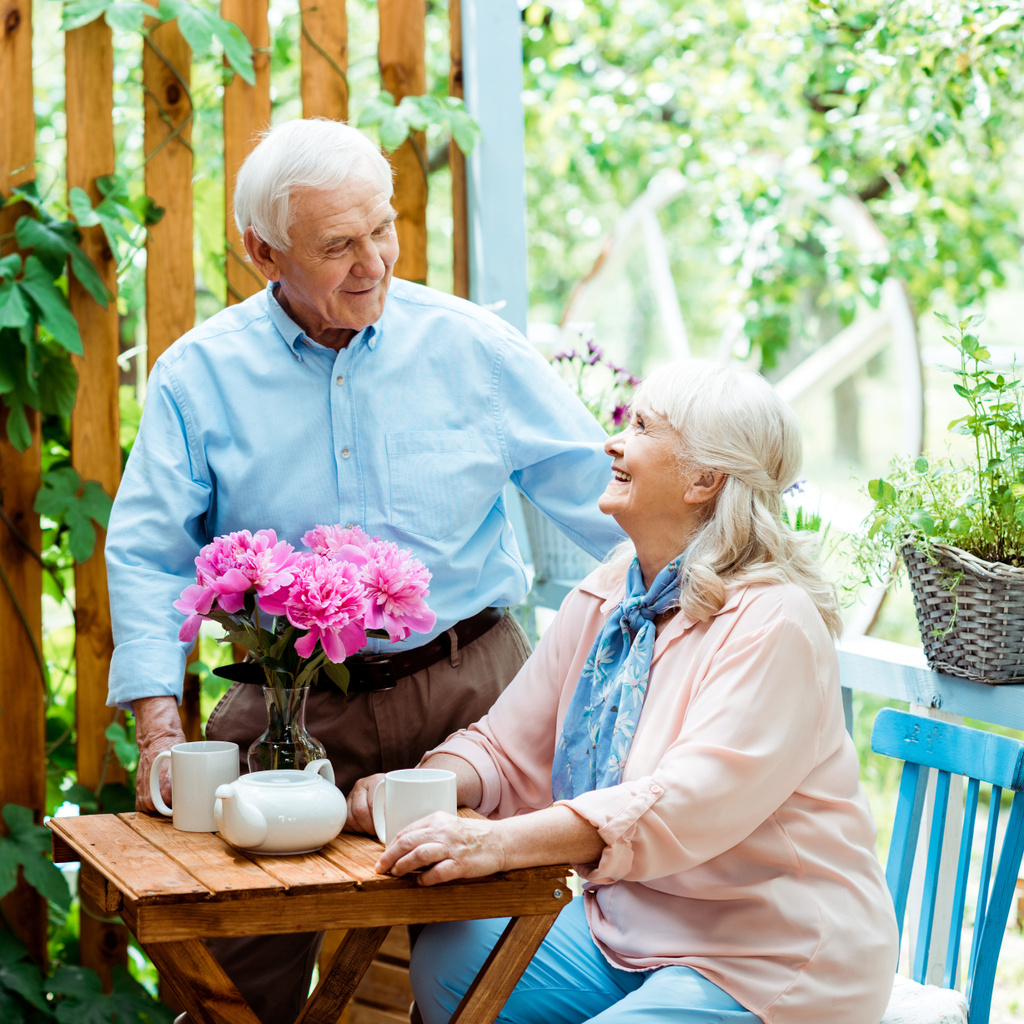 счастливый старший мужчина стоя и глядя на веселую жену возле чашек
  - Фото, изображение