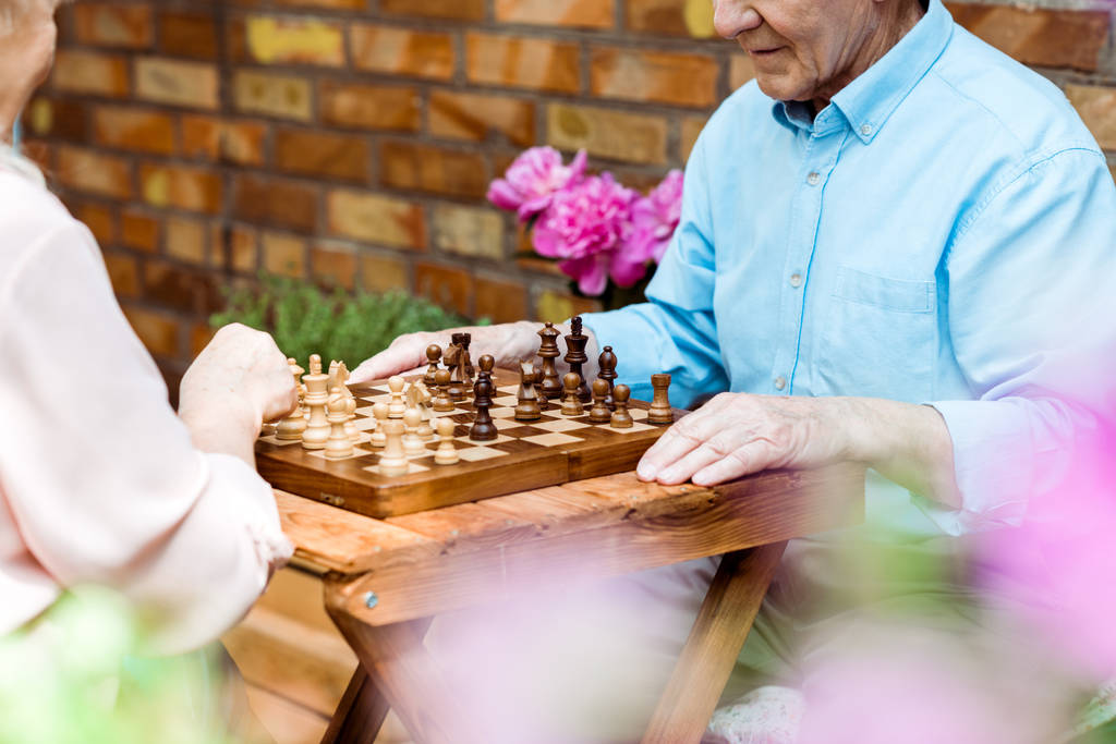 Ausgeschnittene Ansicht eines Rentnerehepaares beim Schachspielen auf einem Holztisch  - Foto, Bild